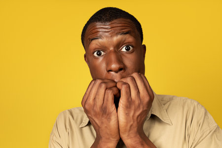 Shocked confused frightened young african american guy in casual bites fingersの写真素材