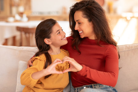 Happy Mother And Daughter Holding Hands In Heart Shape Indoorの写真素材