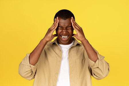 Despaired sad millennial african american guy in casual presses hands to temples, suffering from headacheの写真素材