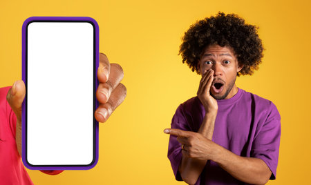 Shocked glad african american young man pointing finger hand with smartphone with empty screen
