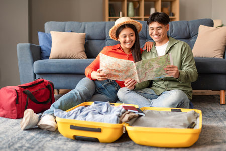Chinese Tourists Couple Looking At Travel Map Near Suitcase Indoorの写真素材