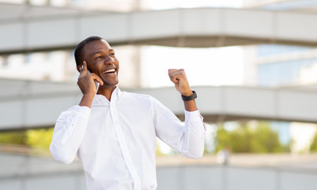 Happy african american businessman talking on cellphone outdoors and celebrating success
