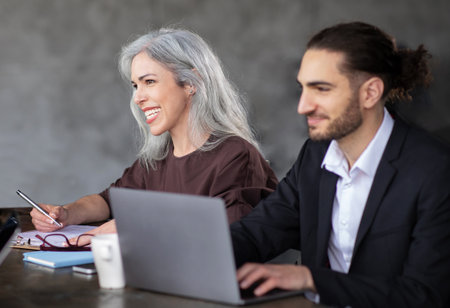 Two colleagues sitting at laptop engaging in business meeting indoor