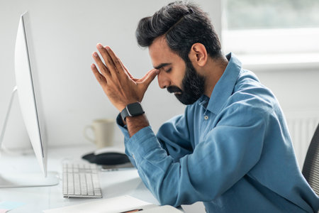 Stressed indian businessman frustrated with work sitting in front of computer at workplace in office