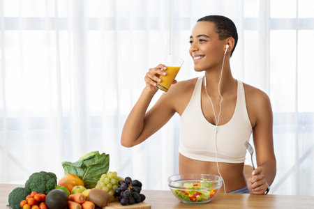 Smiling slim young latin lady in sportswear drink orange juice, eat salad, listen musicの写真素材