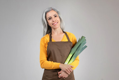 Smiling pretty calm senior woman farmer in apron hold onion leek, enjoy eco green harvestの写真素材