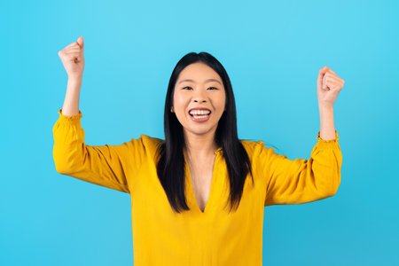 Emotional millennial asian woman raising hands up on blueの写真素材