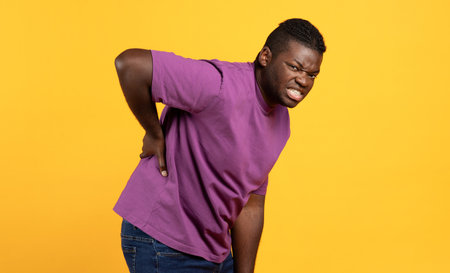 Unhappy black guy touching his aching lower back, yellow backgroundの写真素材