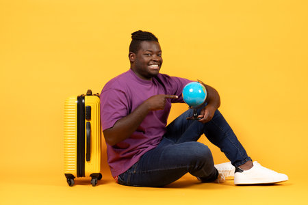 Cheerful African Tourist Guy Sitting Neat Suitcase Holding Globe, Studioの写真素材