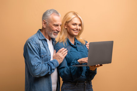 Happy senior couple using laptop, beige background