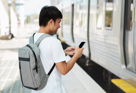 Asian guy student using smartphone, standing by trainの写真素材