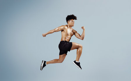 Athletic fit man sprinting and leaping forward on blue backgroundの写真素材