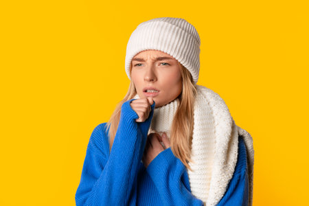 European lady with cough in winter attire, yellow backgroundの写真素材