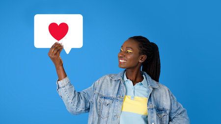 Joyful black millennial woman showcasing social media like, blue background