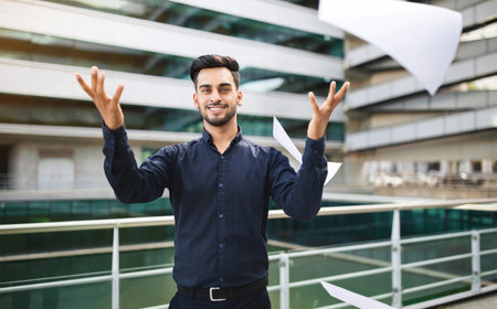 Happy young arab businessman throwing business papers in air outdoorsの写真素材