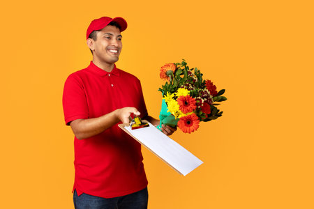 Hispanic deliveryman delivers flower bouquet in studio on yellow backgroundの写真素材