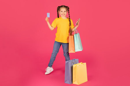 Kids Shopping Concept. Happy Little Girl Holding Purchases, Smartphone And Credit Cardの写真素材