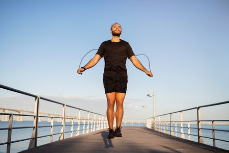 young sportsman with jumping rope exercising at sea pier outdoorsの写真素材