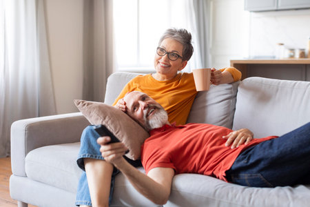 Retirement Pastime. Smiling Elderly Spouses Relaxing On Couch At Homeの写真素材