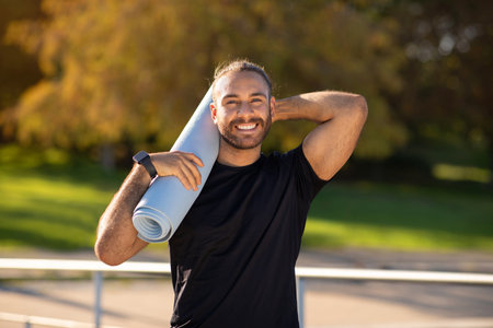Sporty young man holding fitness mat in serene parkの写真素材