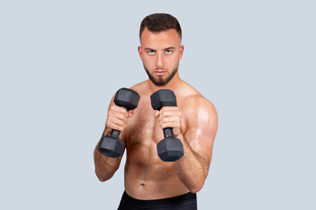Serious sweat muscular young caucasian man athlete with beard, naked torso make exercises with dumbbell for handsの写真素材