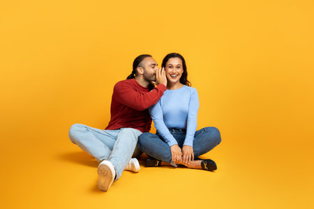 Man sharing secrets with girlfriend, millennial couple on yellowの写真素材