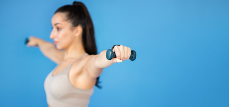 A fit young lady is lifting weights on blue backgroundの写真素材