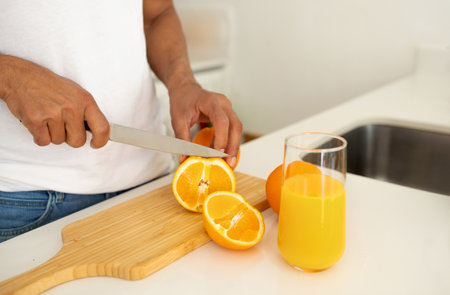 African man slicing oranges for fresh juice in kitchen, croppedの写真素材