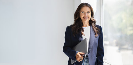 Positive mature woman manager with laptop in her handの写真素材