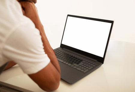 black man using laptop with blank screen at kitchen table