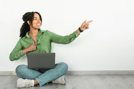 Freelancer Black woman using laptop computer, sits against white wall