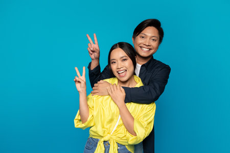 Smiling young korean guy hug lady in casual show peace sign with hands, enjoy relationshipsの写真素材