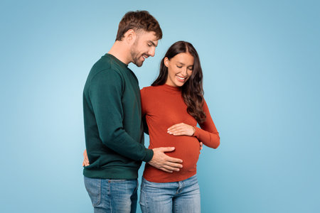 Happy man and woman touching belly, enjoying pregnancy, blue backgroundの写真素材