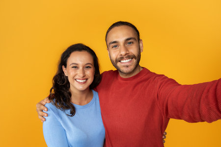 Cute positive young couple taking selfie on yellow backgroundの写真素材