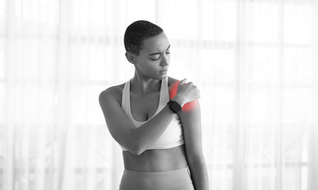 Upset young slim latina woman athlete in sportswear has problems with shoulderの写真素材