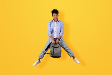 Happy black man mid-jump holding backpackの写真素材