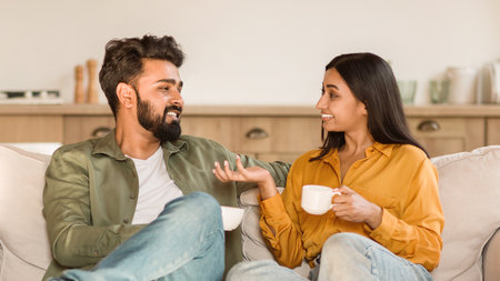Happy indian couple conversing on a couch with coffeeの写真素材