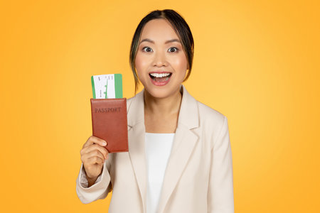 Positive surprised young korean business lady in suit, with open mouth show passport with ticketの写真素材