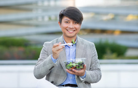 Korean entrepreneur man enjoys salad amidst urban city areaの写真素材