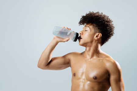 Fit man hydrating after workout posing with water bottle, studio