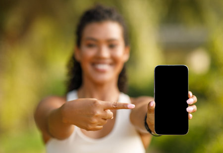 fitness woman in sportswear pointing at blank phone screen outdoorsの写真素材