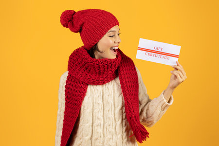 Young woman holding gift certificate card against yellow studio backgroundの写真素材