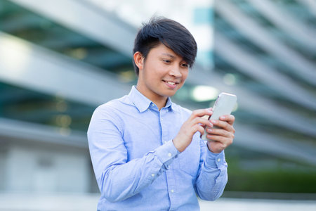 Asian manager messaging and websurfing via smartphone on urban streetの写真素材