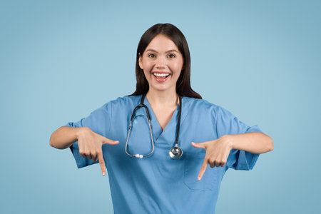 Woman nurse in blue coat points down, smilesの写真素材