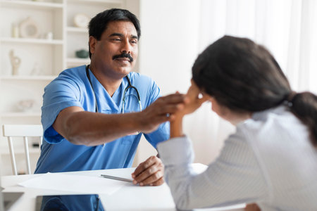 Mature Indian Doctor Man Comforting Depressed Female Patient During Appointment In Clinic