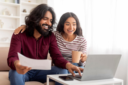 Happy young indian spouses checking papers and counting family budgetの写真素材