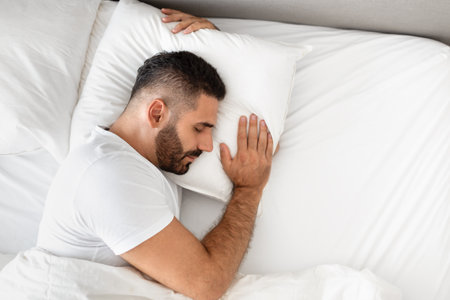 man sleeps in bed hugging pillow for comfort in bedroomの写真素材