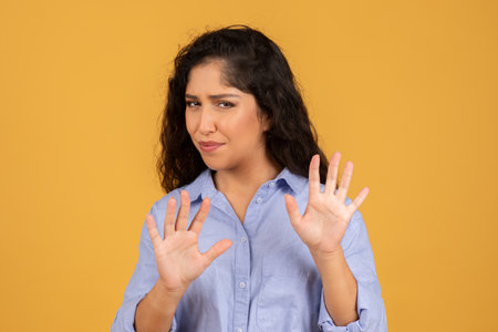 Skeptical young woman in a blue shirt, showing her palms in a defensive stopの写真素材