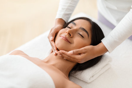 Beautiful young indian woman enjoying face lifting massage in spaの写真素材