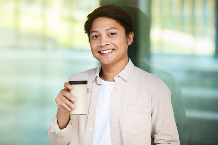 Portrait of cheerful millennial asian man drinking coffee at downtownの写真素材